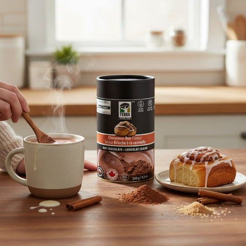 Bean Here Bean There Coffee & Cocoa Terra Cinnamon Bun hot chocolate powder tin with a steaming mug and fresh pastry.